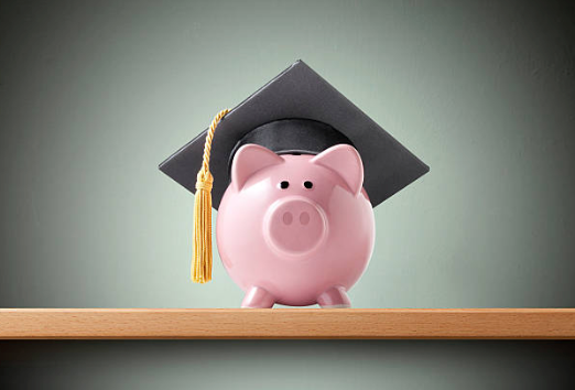 Piggy bank with a graduation cap on top of it sitting on a desk