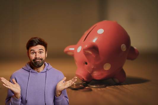 Person, male, who is visually unsure with a piggy bank tipped over behind him on a table with coins in front of the piggy bank