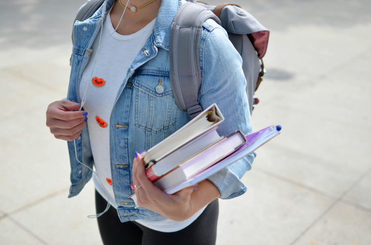 A student walking to class with textbooks listening to music